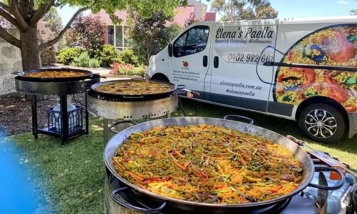 Two large paella pans set up beside the Elena's Paella catering van