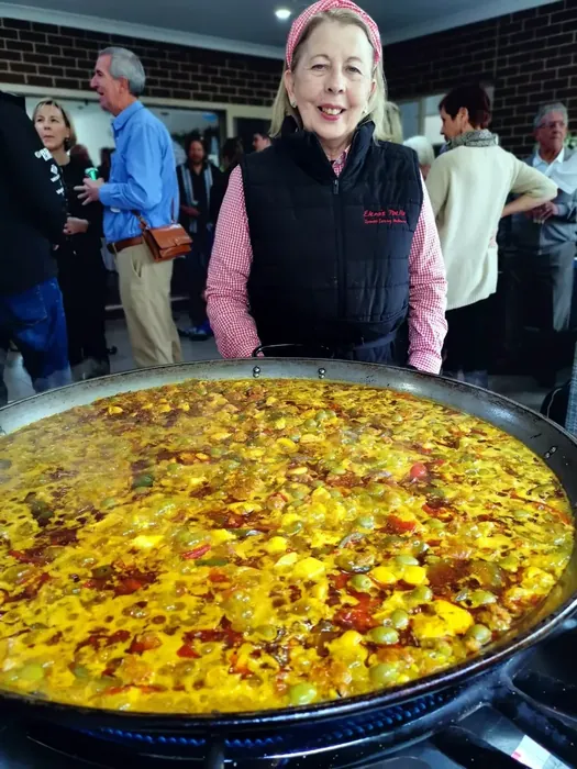 Elena standing behind a large freshly cooked paella