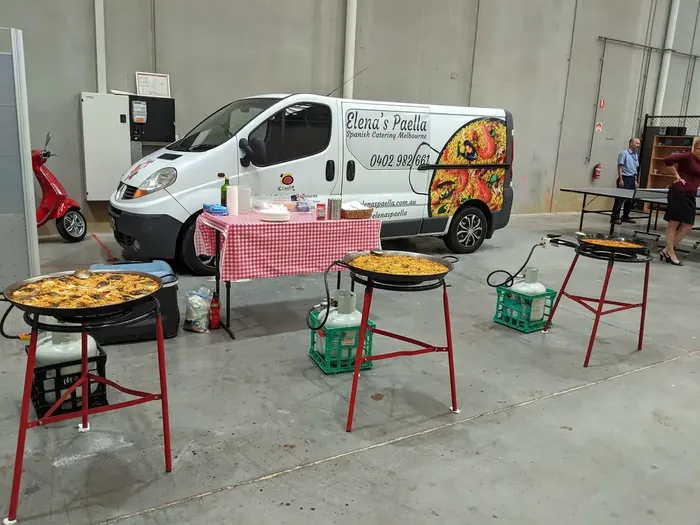 Indoor catering setup with multiple paella pans and equipment